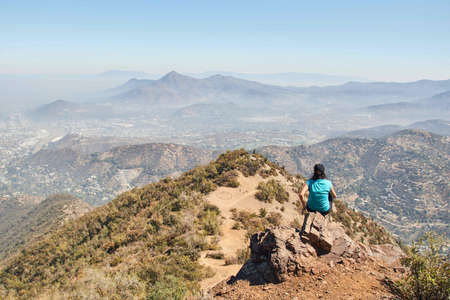 A female sitting on a rock on the edge of a mountain while enjoying the view