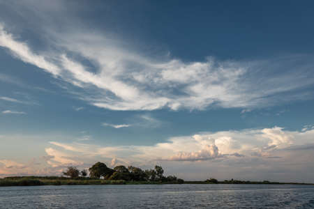 A beautiful scenery of the sea surrounded by  green trees under the cloudy skyの写真素材