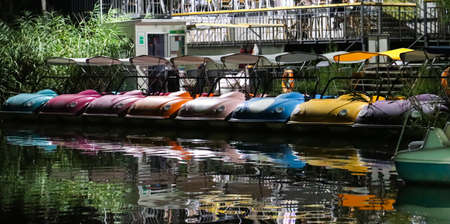 A lot of colorful water pedal vehicles by the water with their reflection in it