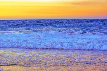 A landscape of a beach surrounded by sea waves during an orange sunset in the evening