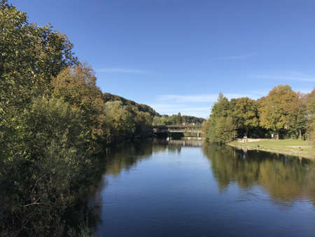 A beautiful shot of a lake in the middle of trees and grassy field and a bridge in the distanceの写真素材