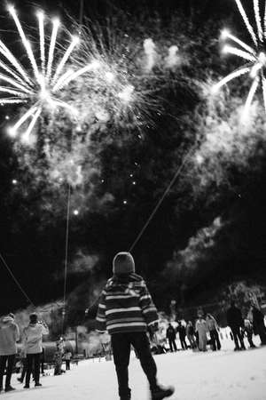 A vertical greyscale shot of a kid admiring the firework in the sky in winterの写真素材