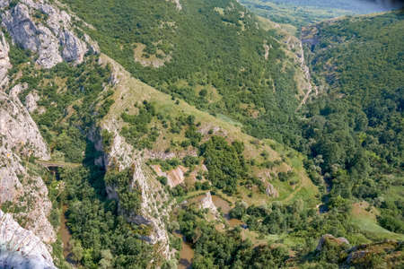 A landscape of rocks covered in greenery under a blue sky and sunlightの写真素材
