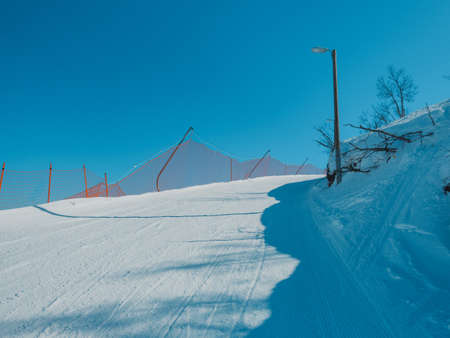 Beautiful scenery of a white snowy road in winter under the clear blue skyの写真素材