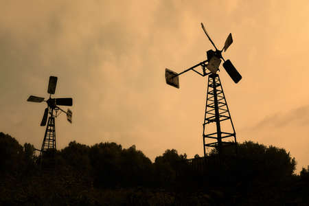 The two iron windmills and the silhouettes of trees under the yellow skyの写真素材