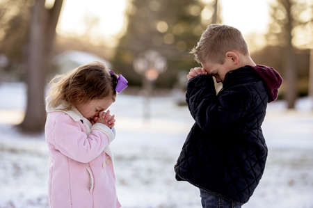 A selective focus shot of cute little kids praying in the middle of a winter parkの写真素材