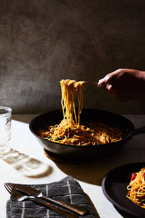 A vertical shot of a person getting some spaghetti from a black pot on a white tableの写真素材