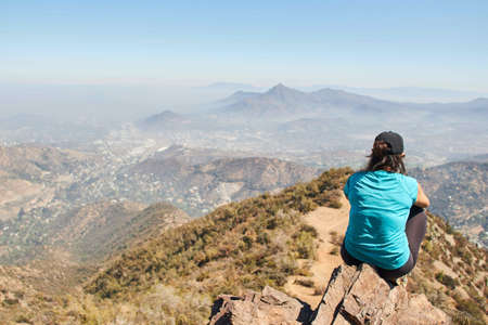 A female sitting on a rock on the edge of a mountain while enjoying the view