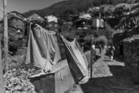 A greyscale of washed clothes on the line surrounded by buildings and hills under the sun