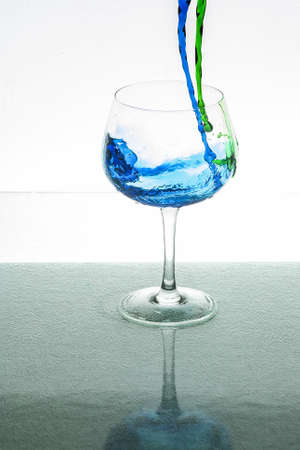 A vertical shot of green and blue liquid pouring in a glass cup with a white backgroundの写真素材