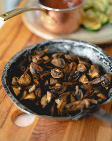 A vertical shot of a pot filled with fried mushrooms on a wooden tableの写真素材