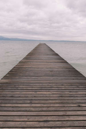 A vertical shot of a wooden pier over the calm ocean under the beautiful cloudy skyの写真素材