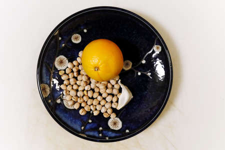 PORTLAND, UNITED STATES - Nov 23, 2019: A high angle shot of some peas and an orange and a garlic on a beautiful plate on a white surfaceの写真素材