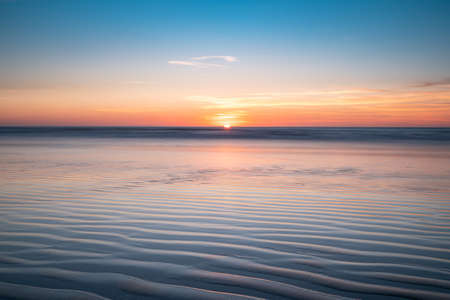 Ocean sunset with ripples of light and shadow that display patterns in the sand.の写真素材