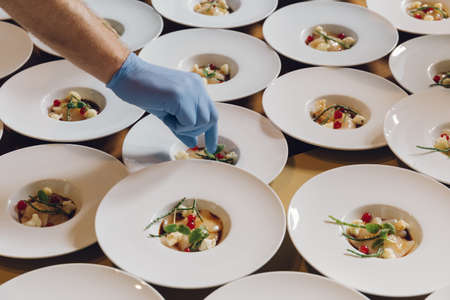 A cook adding ingredients on a dish filled in white serving plates in a restaurantの写真素材