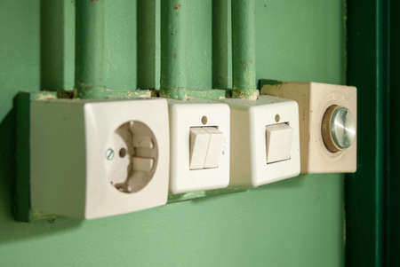 A closeup shot of light switch and light socket on a green wallの写真素材