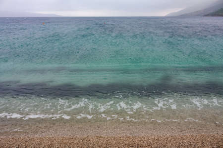 A landscape of a beach surrounded by the sea under a cloudy sky