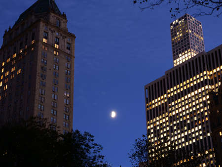 The illuminated buildings and the moon shining in the sky at nightの写真素材