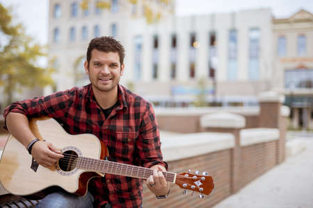 An attractive white male sitting on a bench holding the guitar