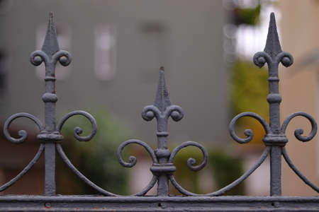 A closeup of a grey metallic fence with buildings and trees on a blurry backgroundの写真素材
