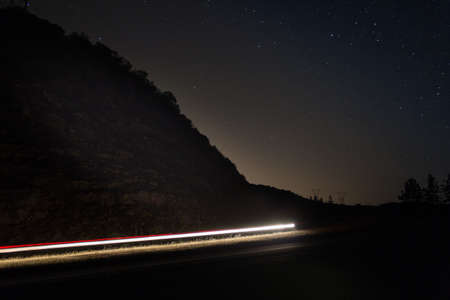 A landscape of a mountain surrounded by trees near a road during the night under a starry skyの写真素材