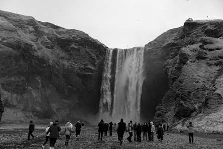 A black and white shot of a group of tourists taking photographs of the tall waterfall in Iceland