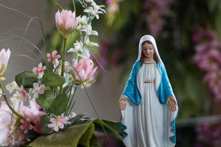 A beautiful small Mary statue next to a fake king protea plant with a blurry backgroundの写真素材