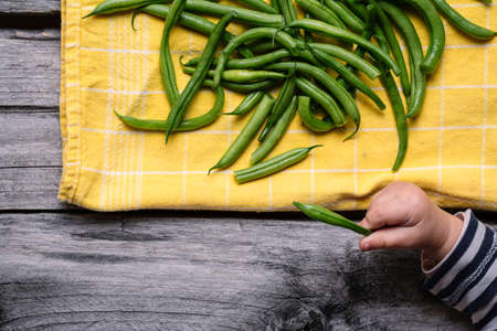 A high angle shot of green beans on a yellow textile and a baby hand playing with themの写真素材