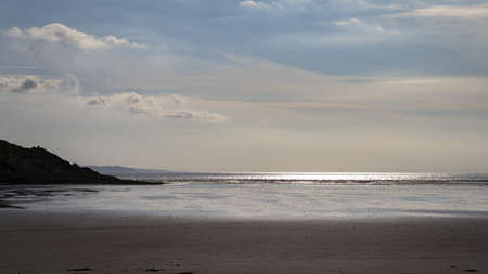 A landscape of a sea from the beach surrounded by hills under a cloudy sky during sunset