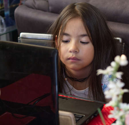 A closeup of a little girl sitting in front of a laptop with a blurry flower in the foreground