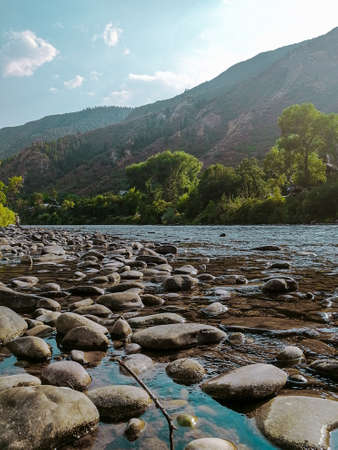 A vertical shot of rocks in the water with a forested mountain in the backgoundの写真素材