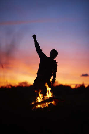 A silhouette of a person dancing with a blurry background and a campfire during a beautiful sunset