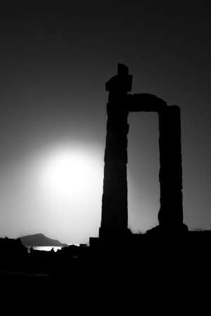 A greyscale of columns of an old temple ruins under sunlight with rocks on the backgroundの写真素材