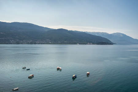 A sea with boats on it surrounded by hills covered in greenery under sunlight