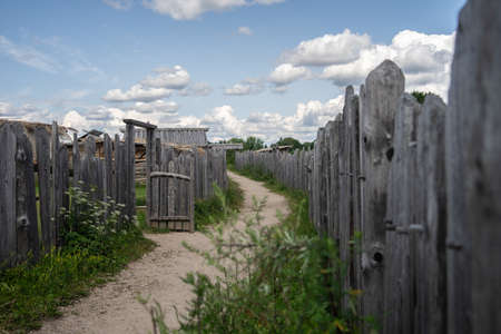 A pathway surrounded by wooden fences and greenery under a cloudy sky during daytime