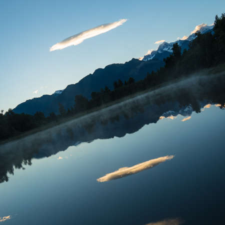 The fluffy white cloud and the mountainous scenery reflecting in the clear lake in New Zealand