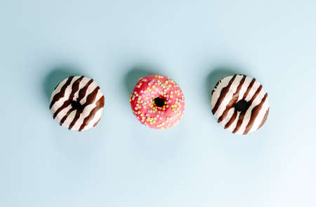 A high angle closeup shot of three donuts on a light blue surface - perfect for a cool wallpaperの写真素材