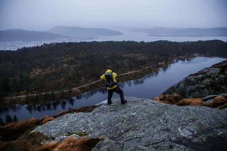 A shot of a hiker standing on a cliff with a river and forest in the backgroundの写真素材