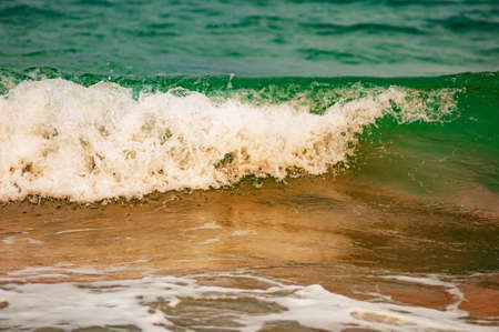 A closeup shot of the foamy turquoise ocean waves soaking the sandy shore