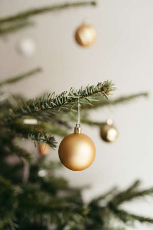 A vertical shot of a Christmas tree decorated with golden baubles against a white wallの写真素材