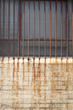 A vertical shot of a rusty weathered window fence on an old brick wallの写真素材