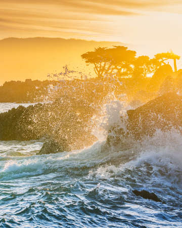 A vertical shot of beautiful sea waves splashing under the sunset skyの写真素材