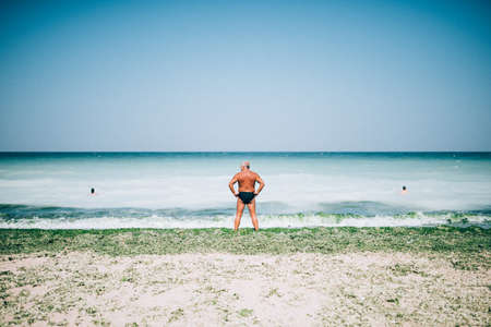 A half-naked white male standing at the ocean shore under the cloudy skyの写真素材