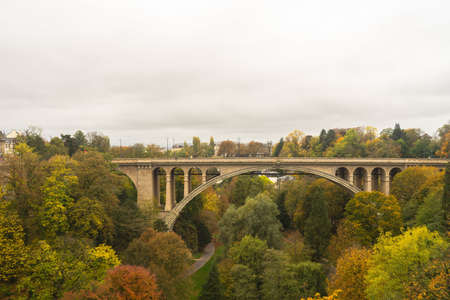 An arch bridge surrounded by trees under a cloudy sky during autumn