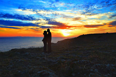 A cute couple kissing at the ocean shore under the breathtaking sunset