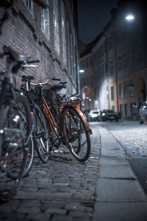 A vertical shot of bicycles parked on the sidewalk in the street at night