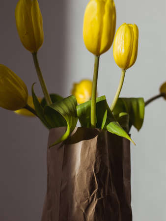 A vertical closeup shot of beautiful yellow tulips in a paper bag with a blurred grey backgroundの写真素材