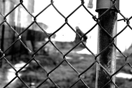 A greyscale closeup of wired fences with buildings under sunlight on the blurry backgroundの写真素材