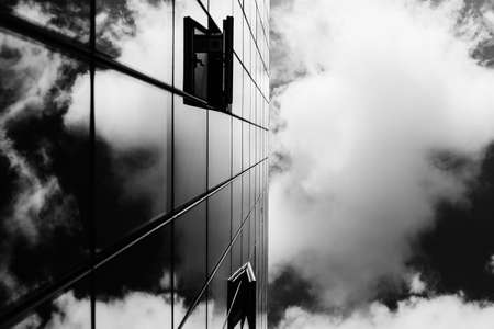 A grey scale shot of a glass tower reflecting the beautiful cloudsの写真素材