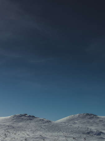 A vertical shot of the snowy hills under the calm pure sky in winterの写真素材